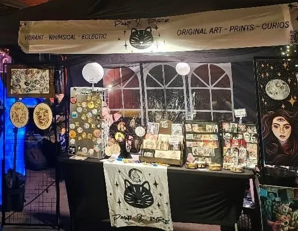 Paint & Pyre market stall at night, with hand painted magnets, prints, and framed originals