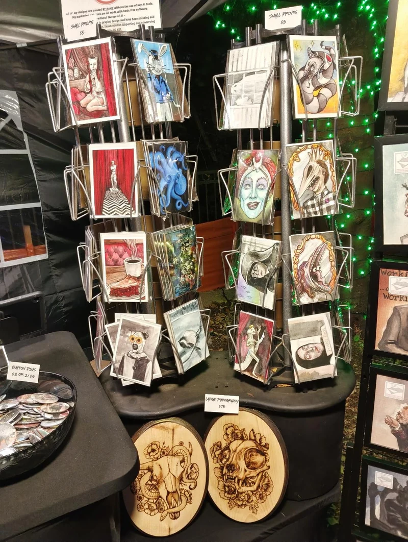 A rotating card display beside two round woodburned artworks on Sara’s market table