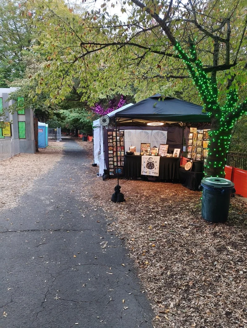 The Paint & Pyre black canopy at an outdoor market beside a tree wrapped in green lights