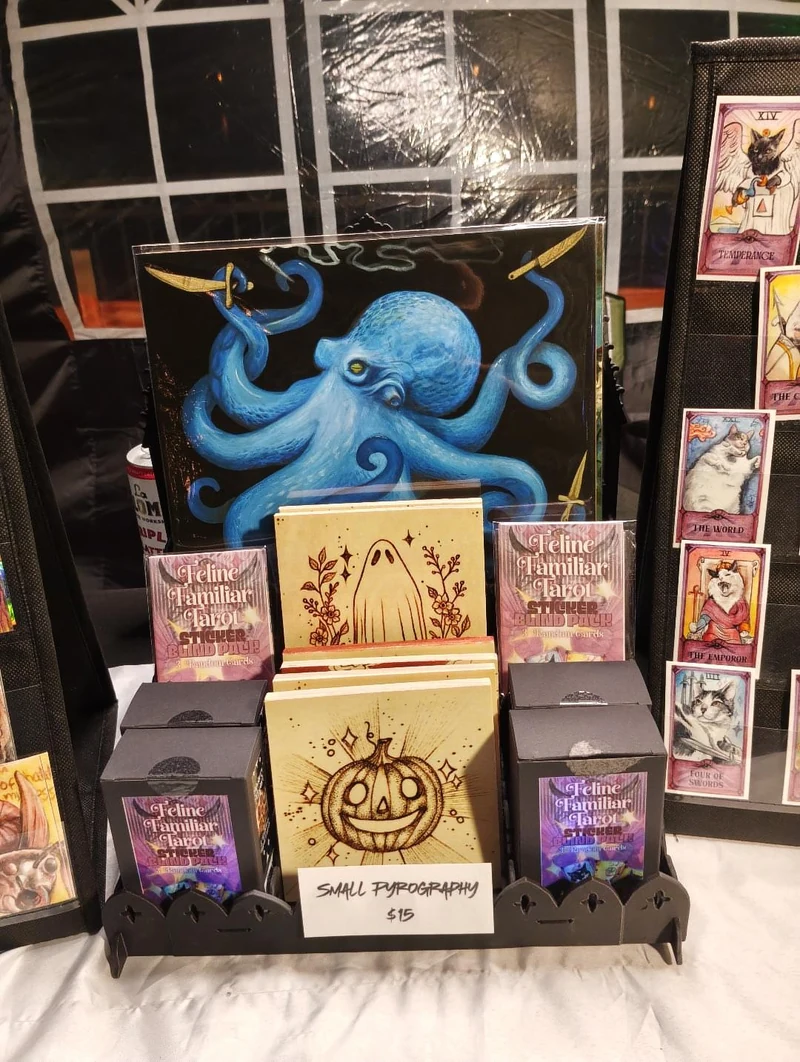 Small woodburned pieces and cards on the table, with a blue octopus painting behind them