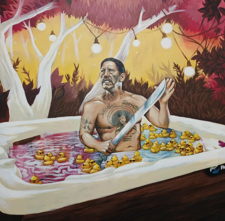 A man sitting in a hot tub holding a machete, surrounded by rubber ducks in sunglasses, under string lights and red autumn trees