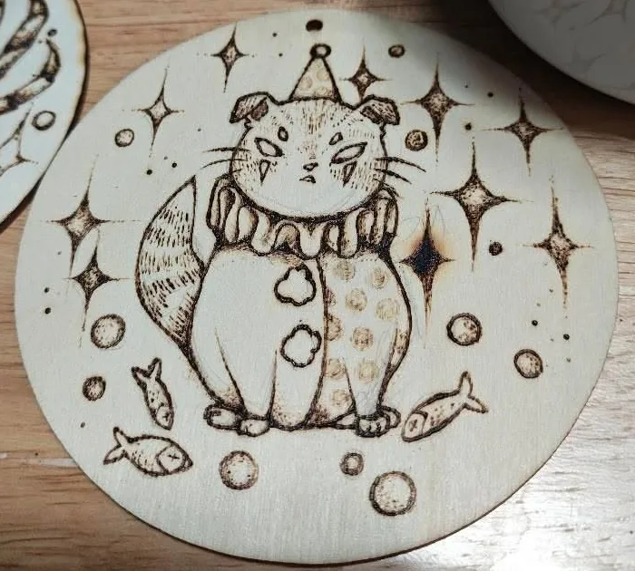 A cat in a ruff and a pointed hat sitting among fish, bubbles and four point stars, burned into a pale round of timber
